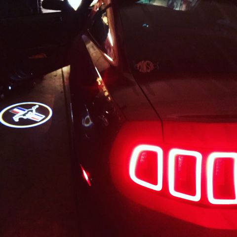 2014 Ford Mustang - The illuminated pony logo projects onto the ground next to the rear of a 2014 Ford Mustang.