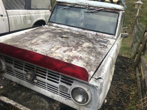 1967 Ford Bronco - A dilapidated 1966 Ford Bronco sits next to a white pickup truck, showing significant wear and tear.