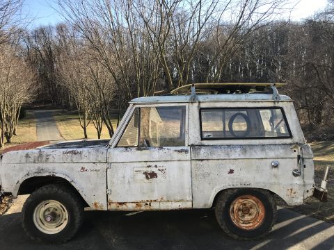 1967 Ford Bronco - This weathered 1967 Ford Bronco sits parked outdoors with a wooded background and a driveway visible.