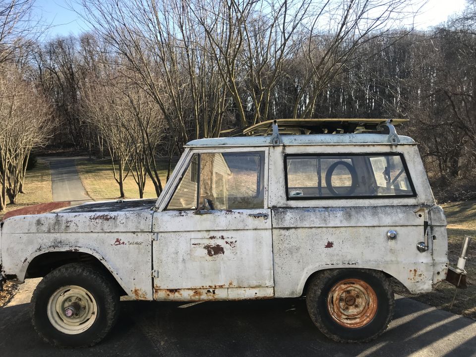 Side view of a white 1967 Ford Bronco with rust and a roof rack