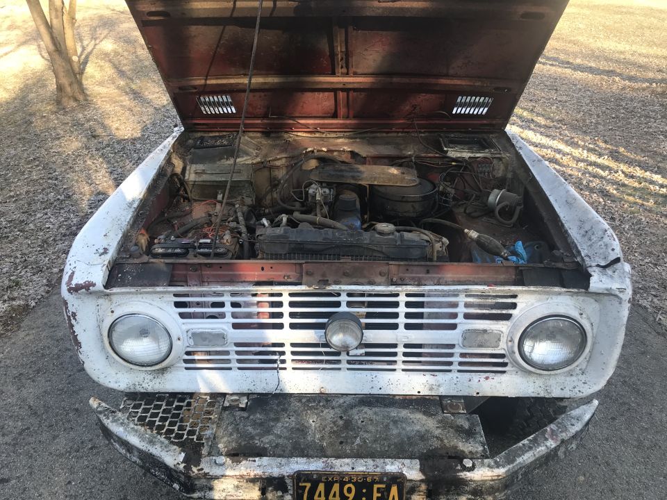 1967 Ford Bronco front view, hood open showing engine bay. Grille and headlights visible