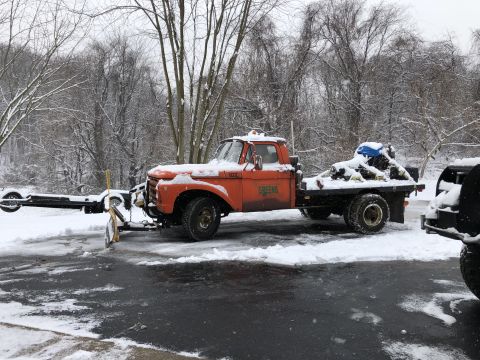 1961 Ford F-350 - Orange 1961 Ford F-350 flatbed truck equipped with a snow plow attachment and carrying a load in the bed during winter.