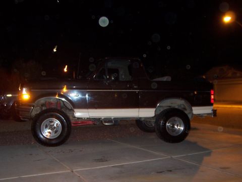 1992 Ford Bronco - Night side view of a dark lifted 1990s Ford Bronco with its fiberglass top removed, leaving the roll bar and open rear tub exposed, parked…
