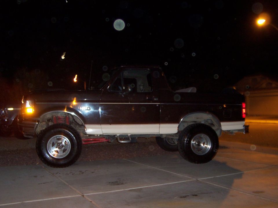 Dark lifted Ford Bronco with top removed, side view on driveway at night