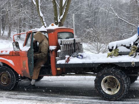 1961 Ford F-350 - A person enters an orange flatbed truck parked in a snowy environment, with a load of bricks visible in the truck bed.