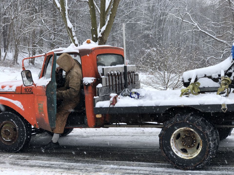 Orange flatbed truck in snow, person in driver's seat, load of bricks in bed