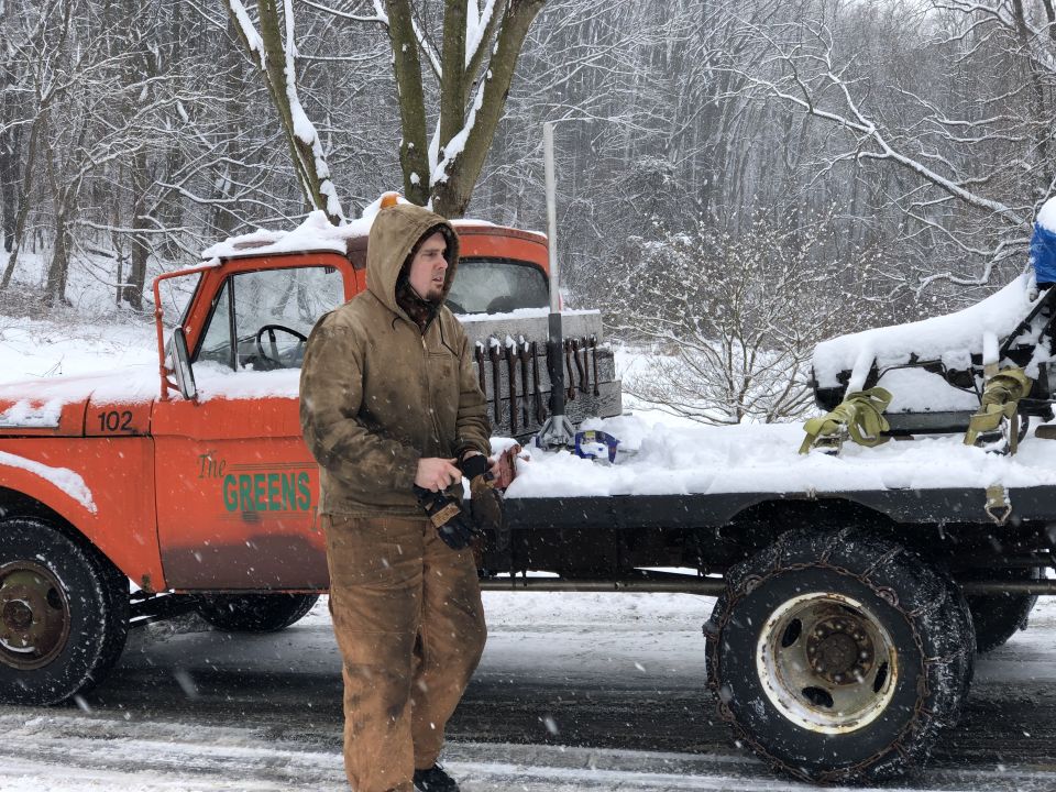 1961 Ford F-350 flatbed truck with a man standing next to it in the snow