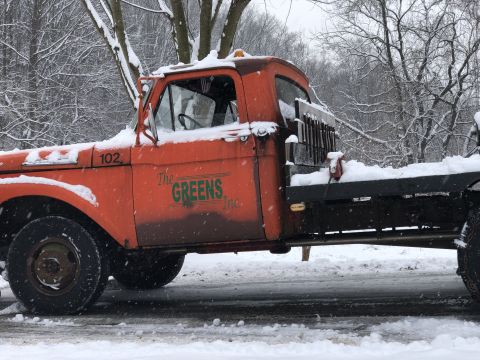 1961 Ford F-350 - An orange flatbed truck, likely from the 1950s, sits covered in snow with snow plow equipment attached.