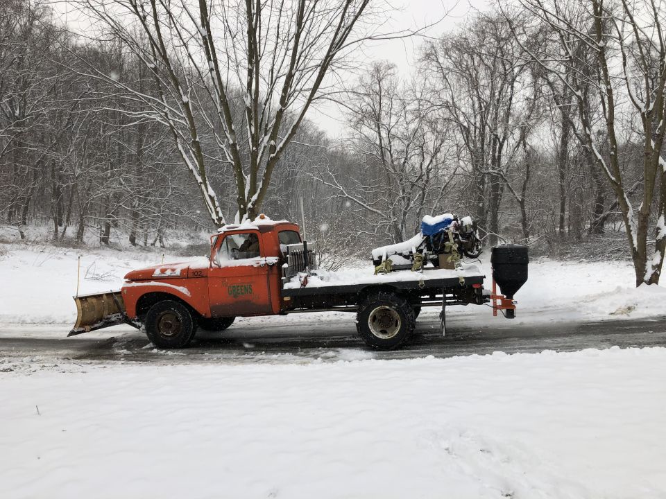 1961 Ford F-350 flatbed truck with front plow and rear salt spreader in snow