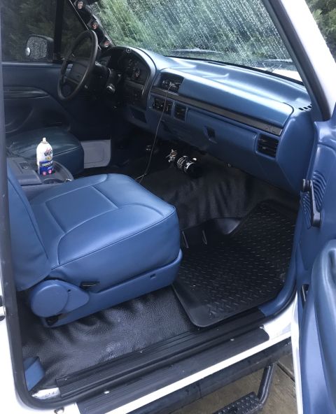 1995 Ford Bronco - The interior of a white SUV shows blue seats and dashboard, with a can of air freshener in the console.