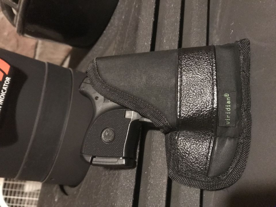 Black handgun in a black holster with "viridian" label, next to a black cylindrical object with orange text