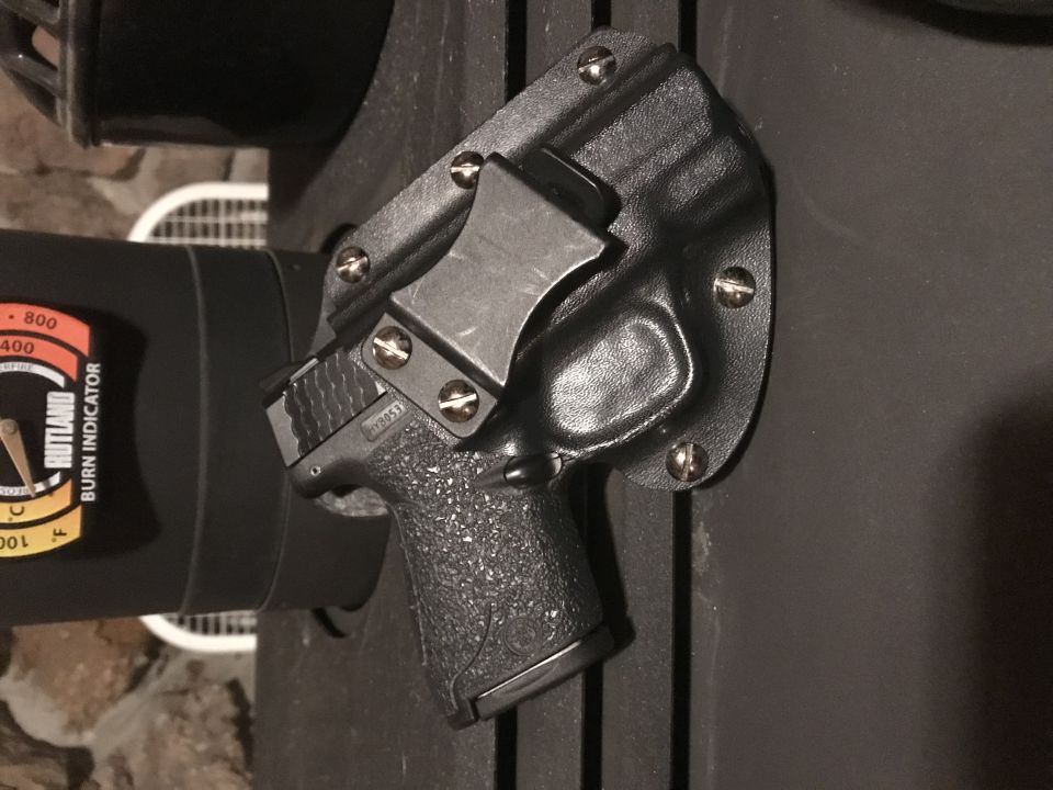 Black handgun in a black Kydex holster attached to a dark surface