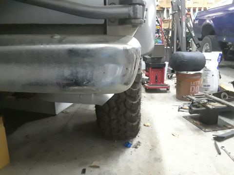 1985 Ford Bronco - Close-up view of a vehicle's rear bumper and tire, with other vehicles and equipment visible in the background.