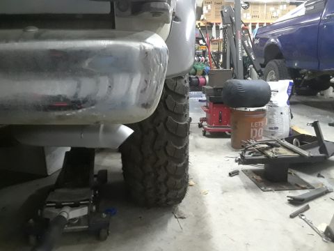 1985 Ford Bronco - Close-up of the rear axle and tire of a 1985 Ford Bronco, with another Ford truck visible in the background.