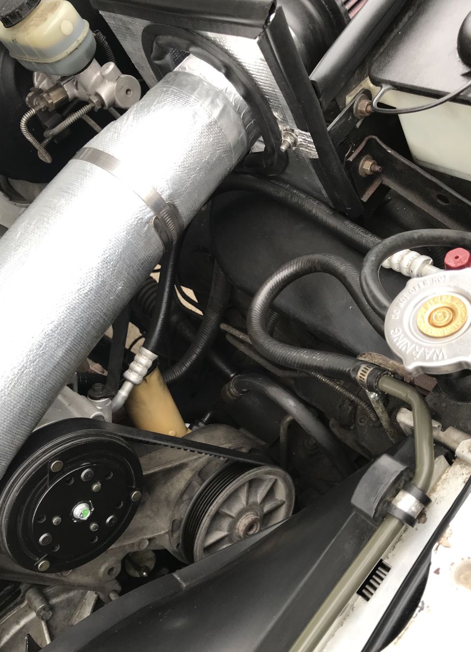 Engine compartment with silver-wrapped intake tube, black hoses, and serpentine belt system