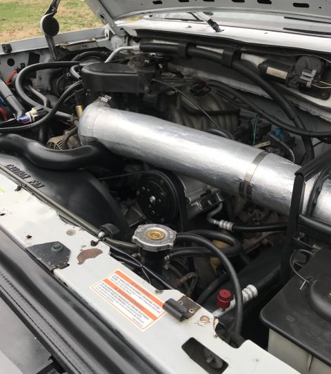 1995 Ford Bronco - The engine bay of a white vehicle, a prominent silver intake pipe and numerous hoses and components.