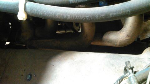 1978 Ford Bronco - A close-up view of engine components, including exhaust pipes and a heater hose.