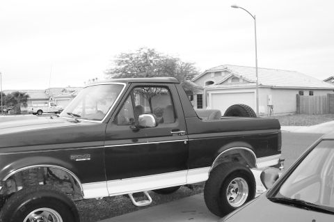 1992 Ford Bronco - Black-and-white side shot of a lifted Ford Bronco with its hardtop removed, showing the open rear tub, roll bar area and Bronco fender badg…