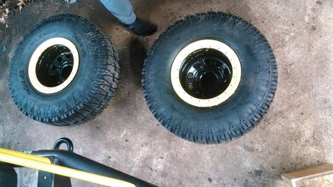 1978 Ford Bronco - Two off-road tires with black rims and cream trim rings are shown on a concrete surface.
