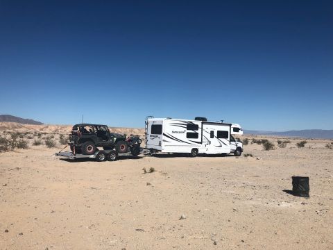 1992 Jeep Wrangler - A black Jeep Wrangler is transported on a trailer behind a white recreational vehicle in a dry, arid environment under a clear blue sky.