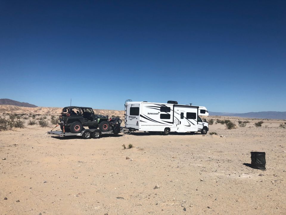 Black Jeep Wrangler on a trailer towed by a white RV in a desert landscape