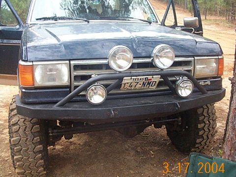 1986 Ford Bronco - This dark blue SUV features a brush guard with multiple off-road lights and a Texas license plate.