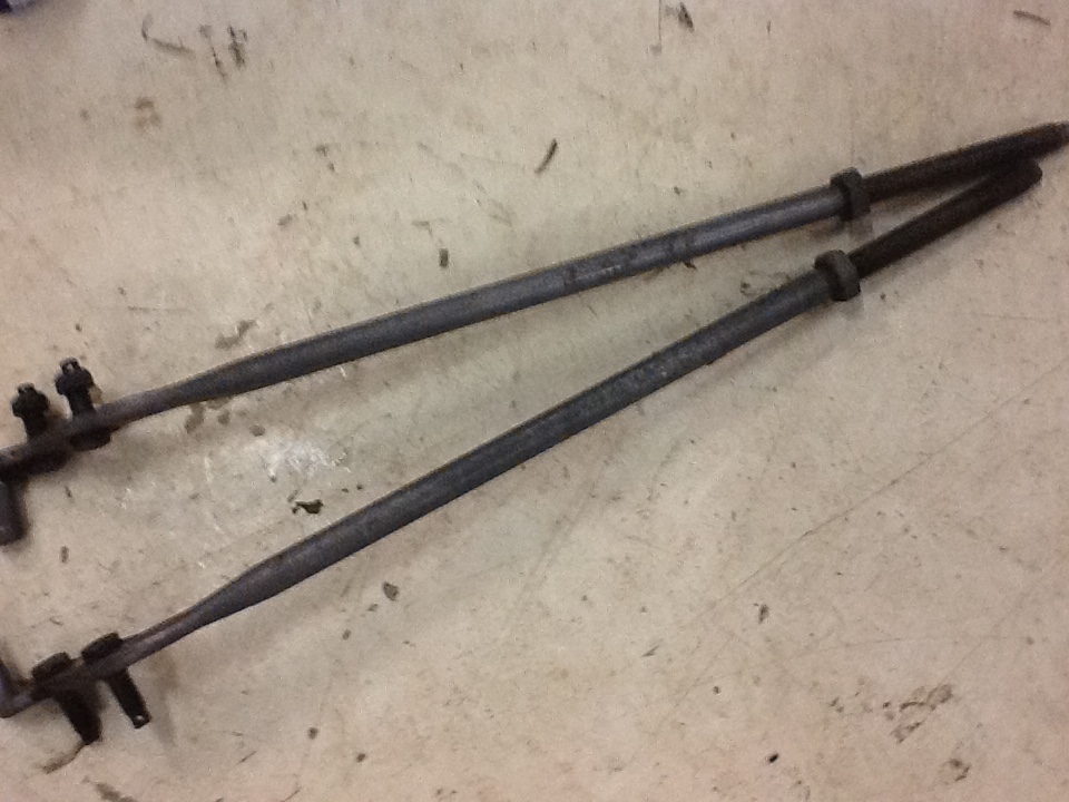 Two used tie rod linkage bars with adjuster sleeves lying on a shop floor