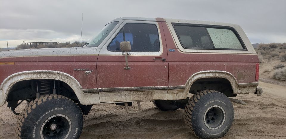 1981 Ford Bronco with lifted suspension and large tires parked on a dirt road