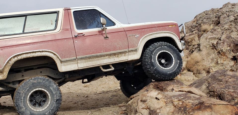 Red and white 1981 Ford Bronco climbing rocks, side view