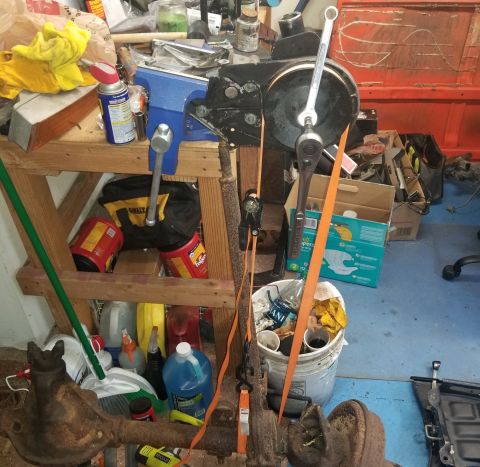 1993 Ford Bronco - A cluttered workbench holds tools and automotive parts, including a vise and a rusty axle.