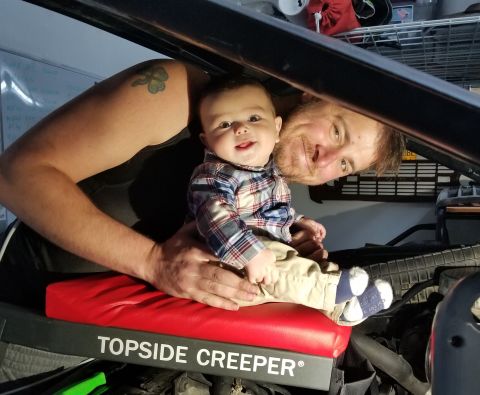 1993 Ford Bronco - A man and a baby are pictured under the hood of a 1993 Ford Bronco, with the text "TOP SIDE CREEPER" visible on a red mat.