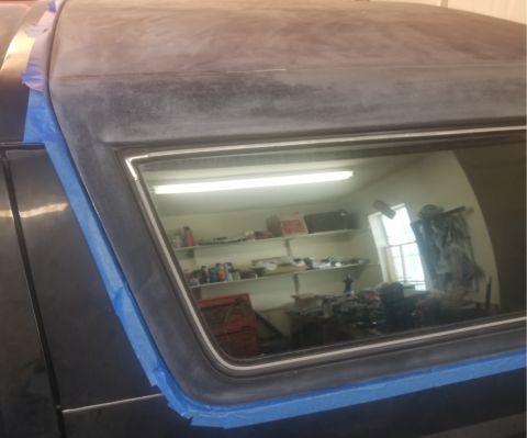 1993 Ford Bronco - A car's roof and window frame, prepped with masking tape, reflect a cluttered workshop environment.