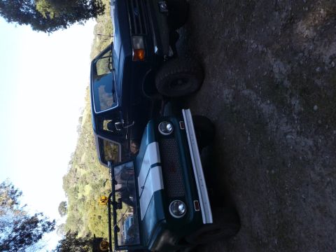 1991 Ford Bronco - Two off-road vehicles, a Ford Bronco and a Jeep CJ-7, are parked outdoors on a dirt lot.