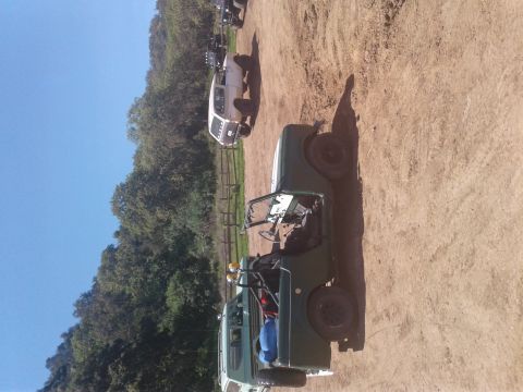 1991 Ford Bronco - Several off-road vehicles are parked on a dirt lot with trees and a blue sky in the background.