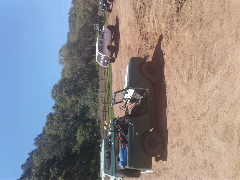 Green off-road vehicle with open top and roll cage parked on dirt