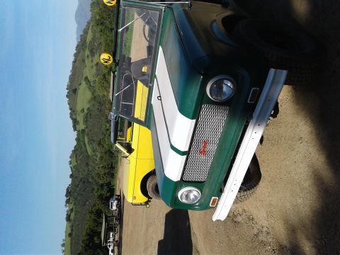 1991 Ford Bronco - A green International Harvester Scout is parked next to a yellow truck on a dirt road with hills in the background.
