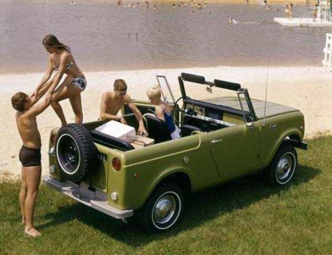 1991 Ford Bronco - People gather around a vintage green convertible SUV parked on grass near a lake.