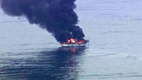 1991 Ford Bronco - A boat is on fire and emitting thick black smoke while floating on the water.