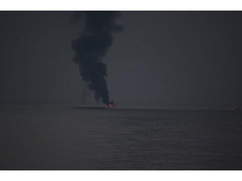 Burning vehicle emitting black smoke against a dark, hazy background