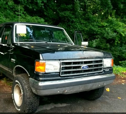 1988 Ford Bronco - This black 1988 Ford Bronco features a prominent Ford grille and distinctive headlights, captured in a three-quarter front view.