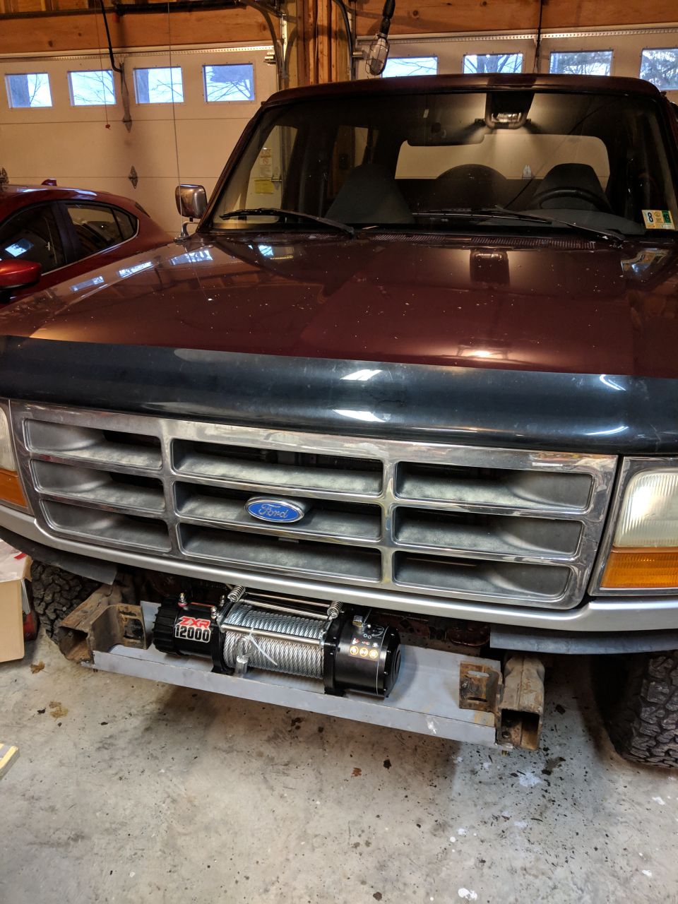 Front of a 1990s Ford truck with chrome grille and mounted winch in a garage