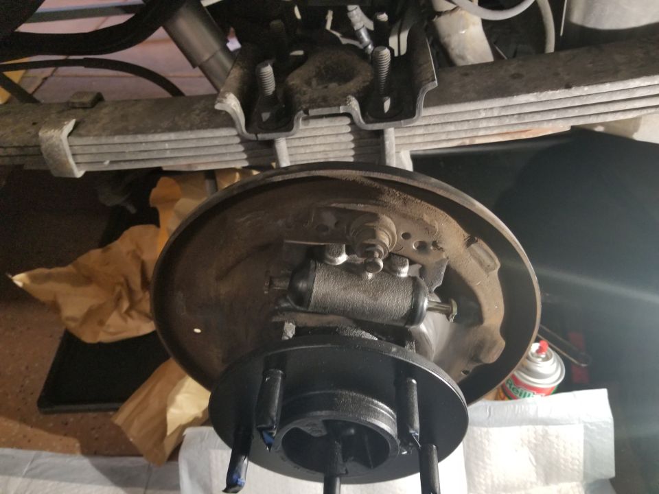 Rear drum brake assembly with leaf springs above. A can of spray paint is visible to the right