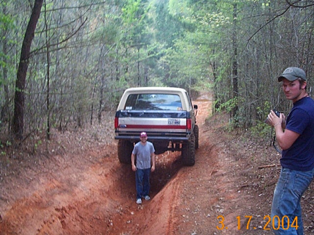Rear view of a lifted Ford Bronco on a dirt trail, with two men nearby