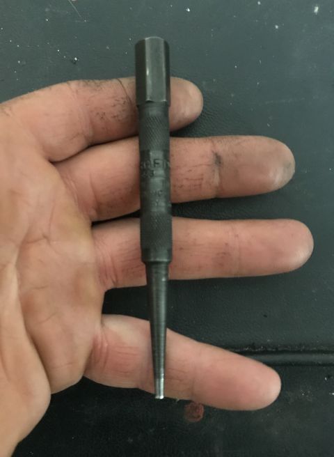 1995 Ford Bronco - A center punch is held in a hand, with visible text on the tool's shaft.