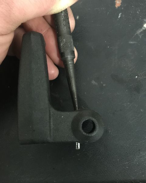 1995 Ford Bronco - Hand using a punch tool on a black metal bracket.