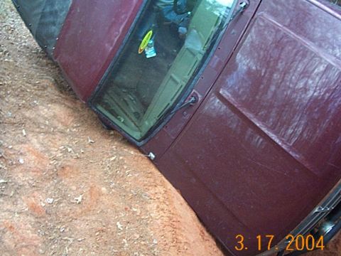 1986 Ford Bronco - This maroon SUV appears to be stuck in a dirt ditch, tilted to its side.