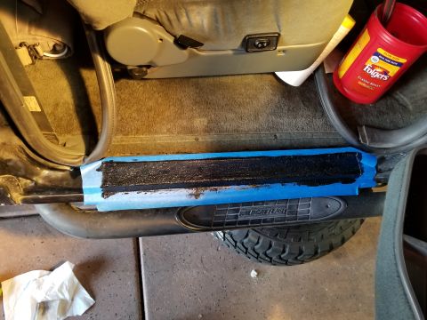 1993 Ford Bronco - The door sill of a vehicle is being prepped for a coating, with blue tape protecting the surrounding area.