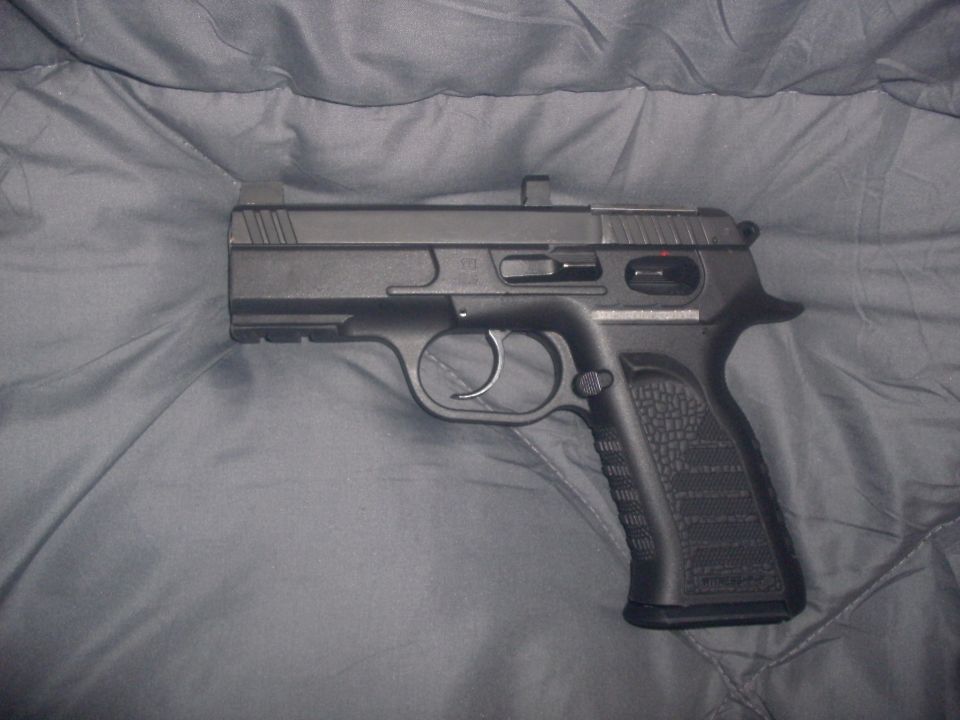 Black semi-automatic pistol on a gray blanket. Text on the bottom right reads "SUPERMOTORS www.supermotors.net"