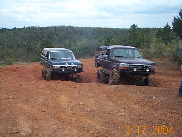 Purple lifted Ford F-150 truck navigating a dirt hill, with a blue Ford Bronco behind it