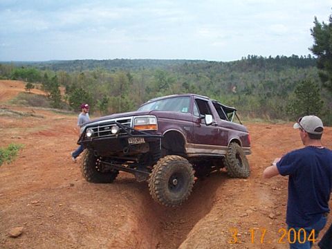 1986 Ford Bronco - A modified Ford Bronco tackles a challenging off-road course with spectators watching.